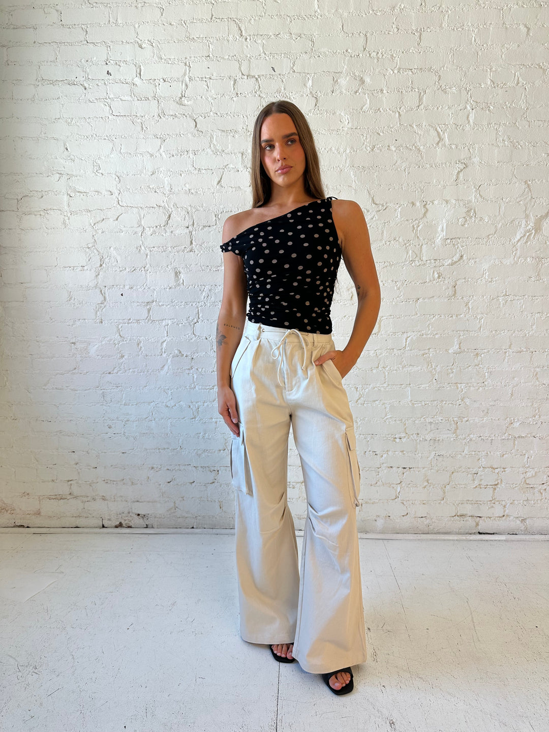 Woman wearing black mesh polka dot top with twist off the shoulder neckline and khaki cargo pant. 