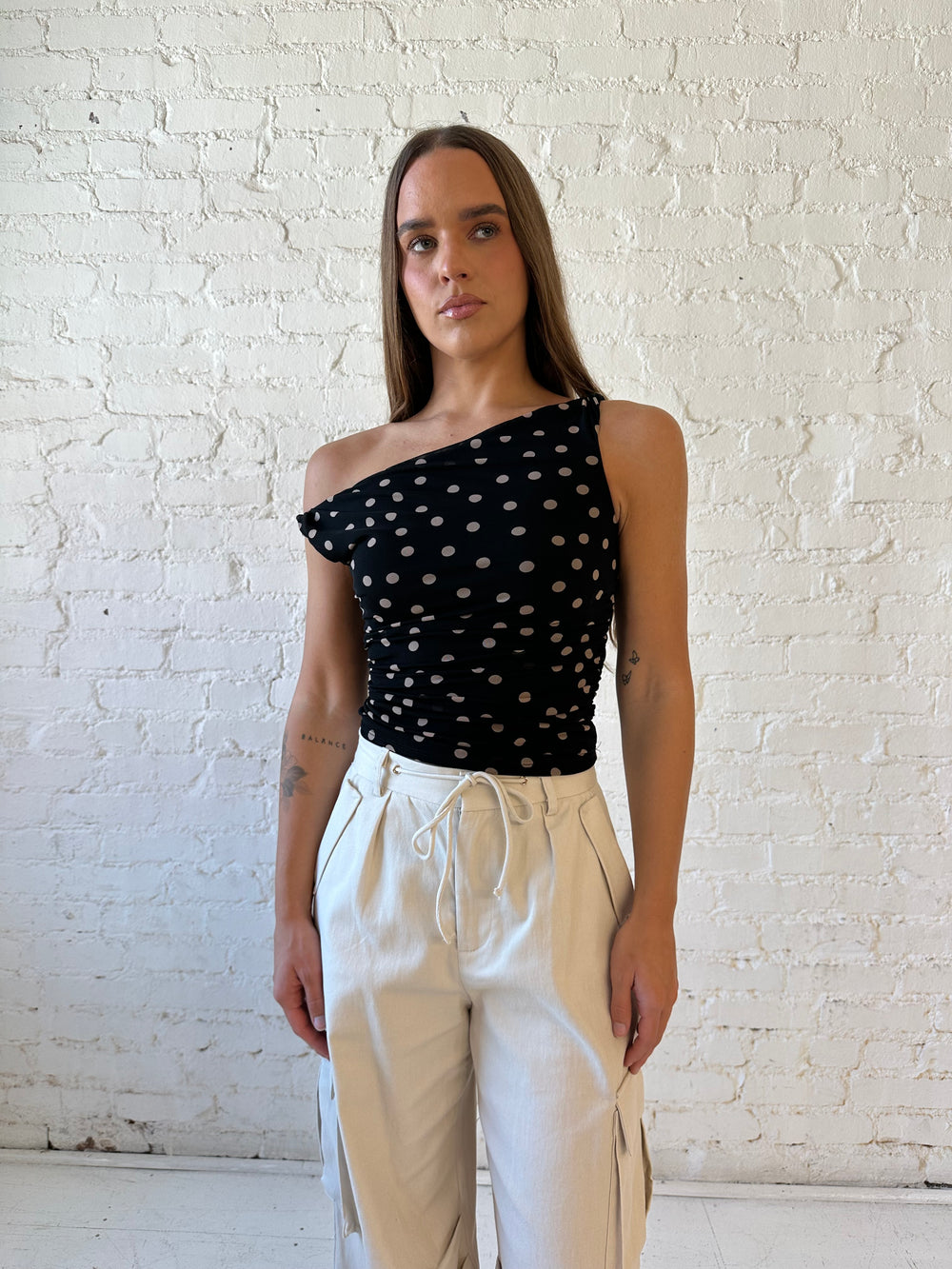 Woman wearing black mesh polka dot top with twist off the shoulder neckline and khaki cargo pant. 