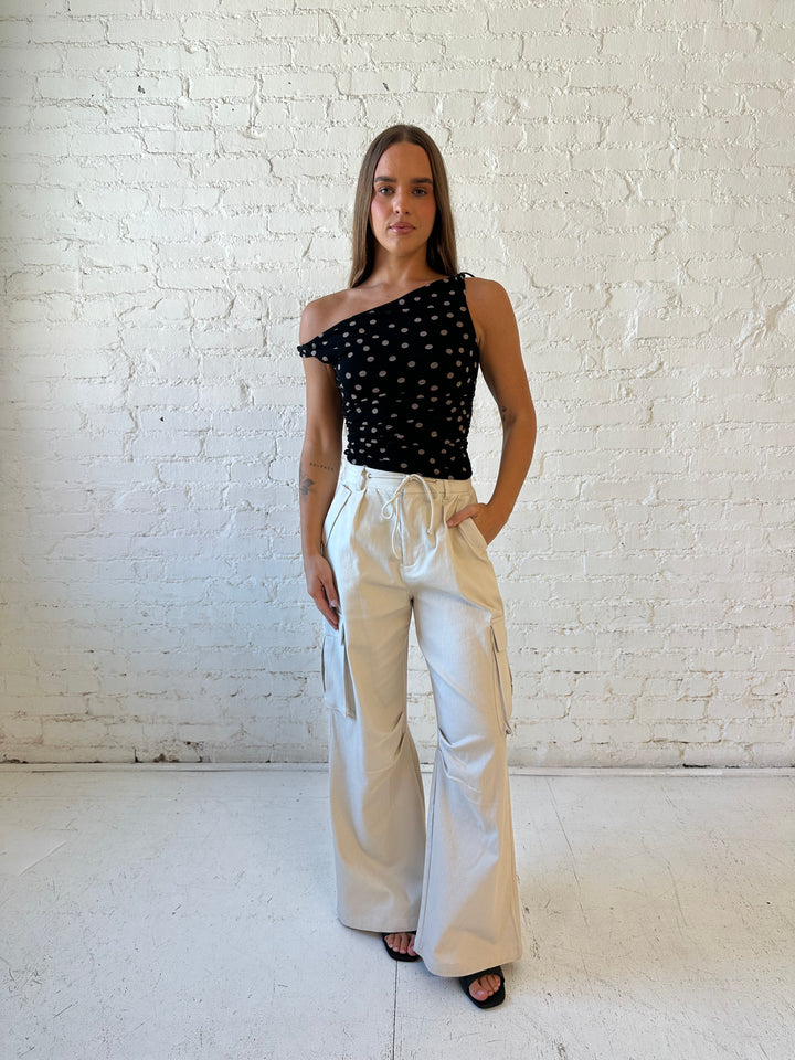 Woman wearing black mesh polka dot top with twist off the shoulder neckline and khaki cargo pant. 