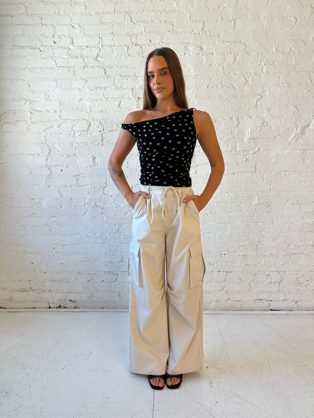Woman wearing black mesh polka dot top with twist off the shoulder neckline and khaki cargo pant. 
