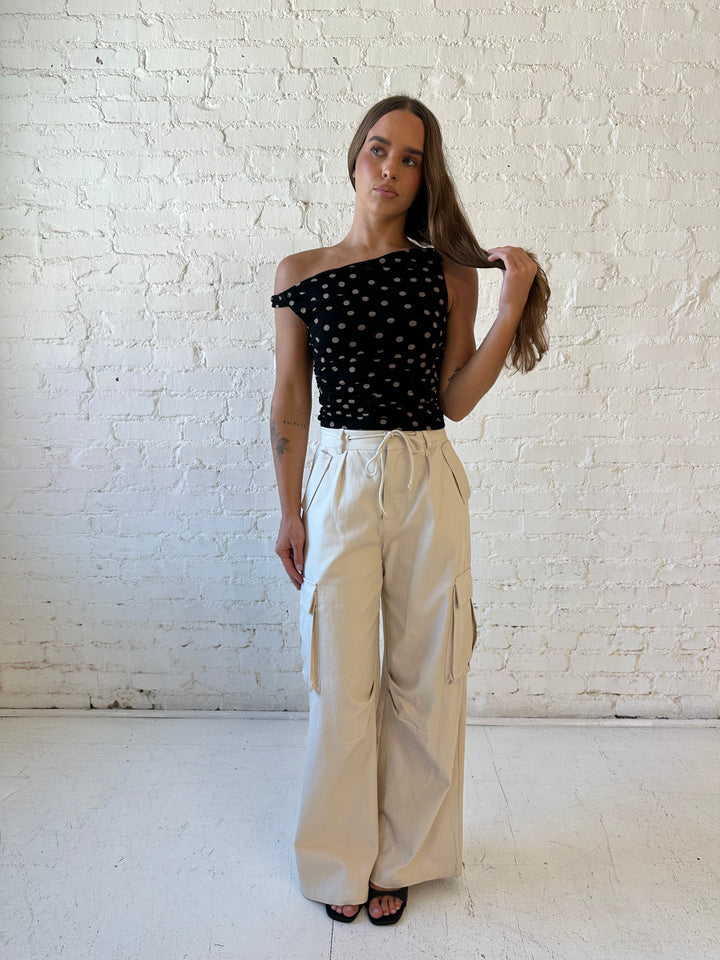 Woman wearing black mesh polka dot top with twist off the shoulder neckline and khaki cargo pant. 