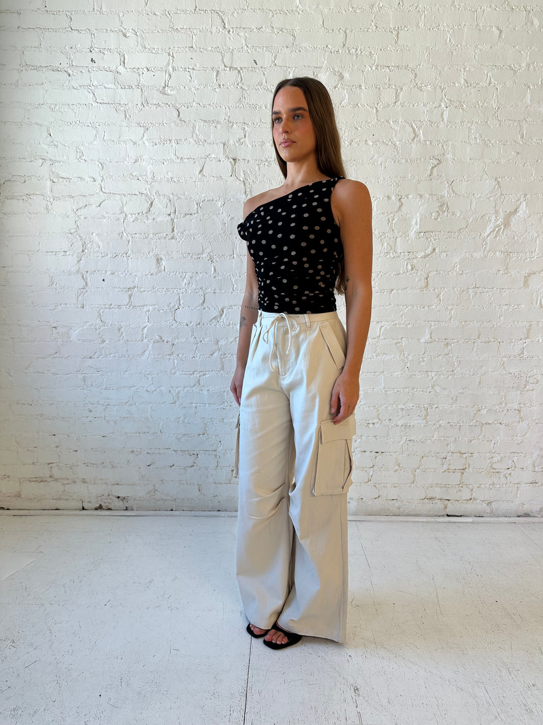 Woman wearing black mesh polka dot top with twist off the shoulder neckline and khaki cargo pant. 