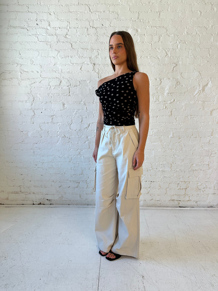 Woman wearing black mesh polka dot top with twist off the shoulder neckline and khaki cargo pant. 