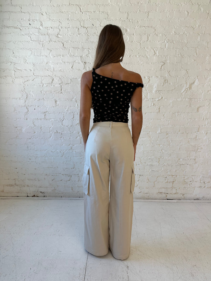 Woman wearing black mesh polka dot top with twist off the shoulder neckline and khaki cargo pant. 