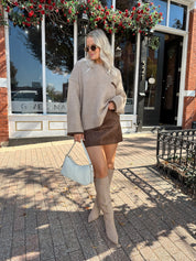 Woman wearing oversized taupe knit sweater with mocha trim detailing.