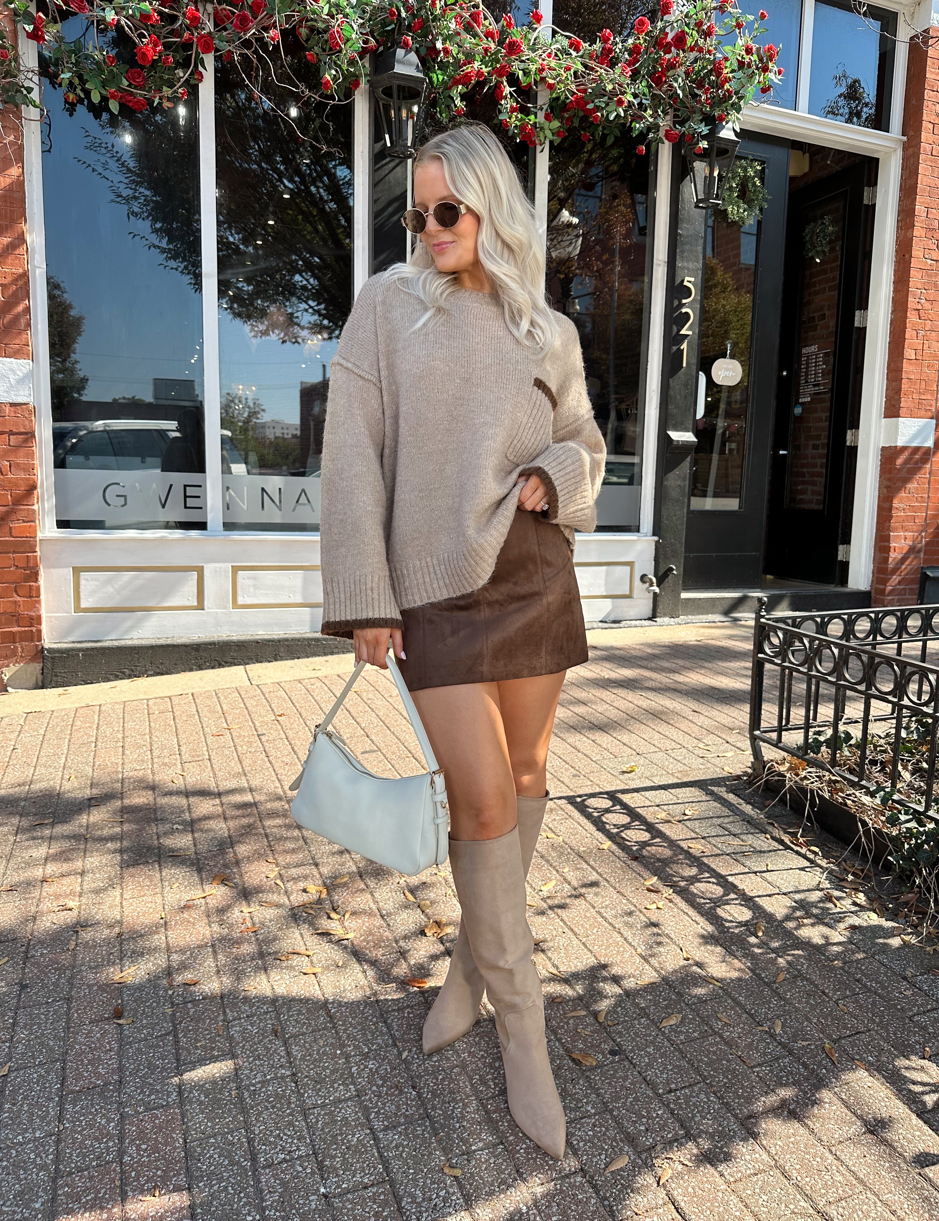 Woman wearing oversized taupe knit sweater with mocha trim detailing.