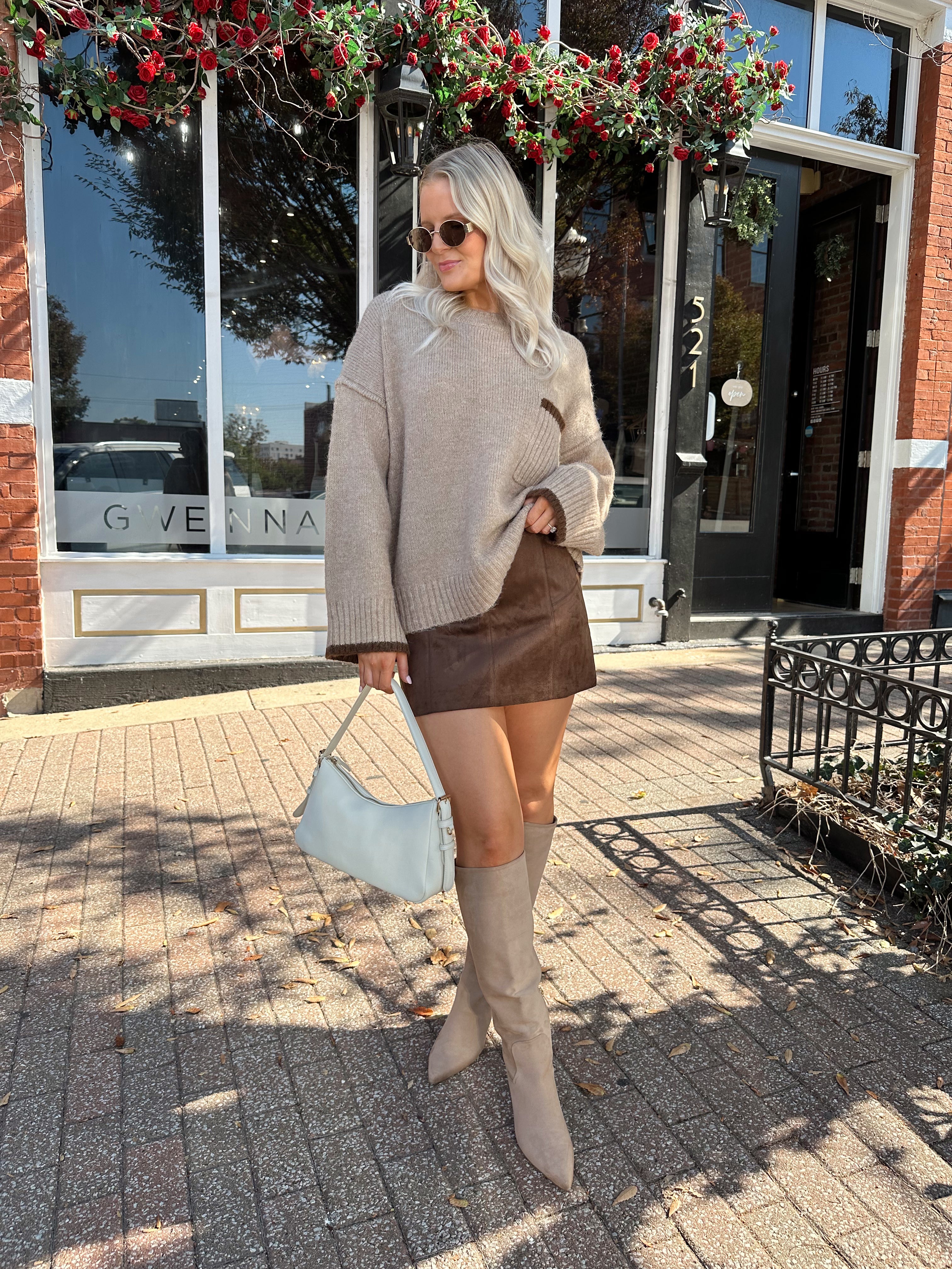 Woman wearing oversized taupe knit sweater with mocha trim detailing.