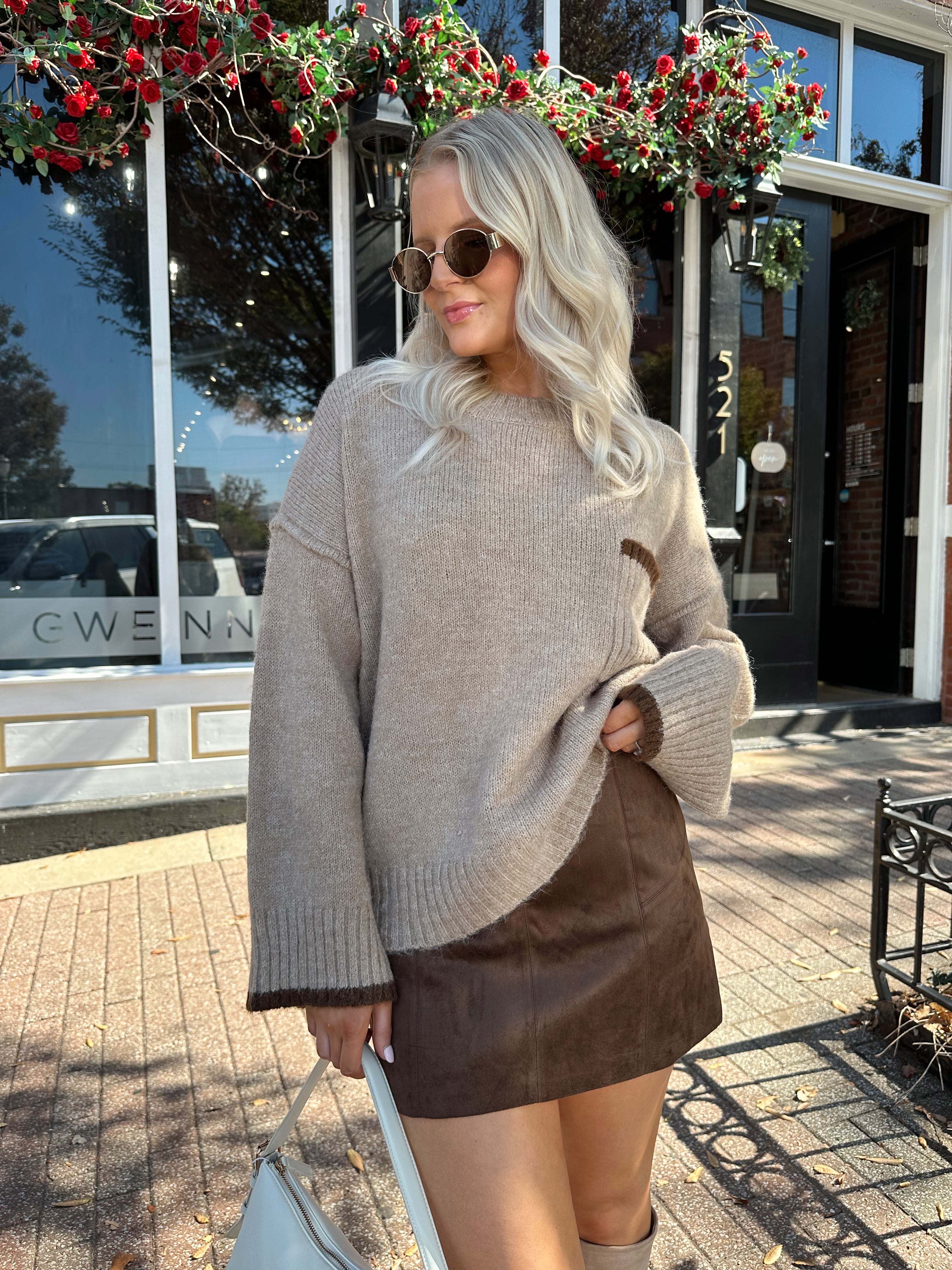 Woman wearing oversized taupe knit sweater with mocha trim detailing.