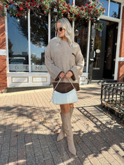 Woman wearing oversized taupe knit sweater with mocha trim detailing.
