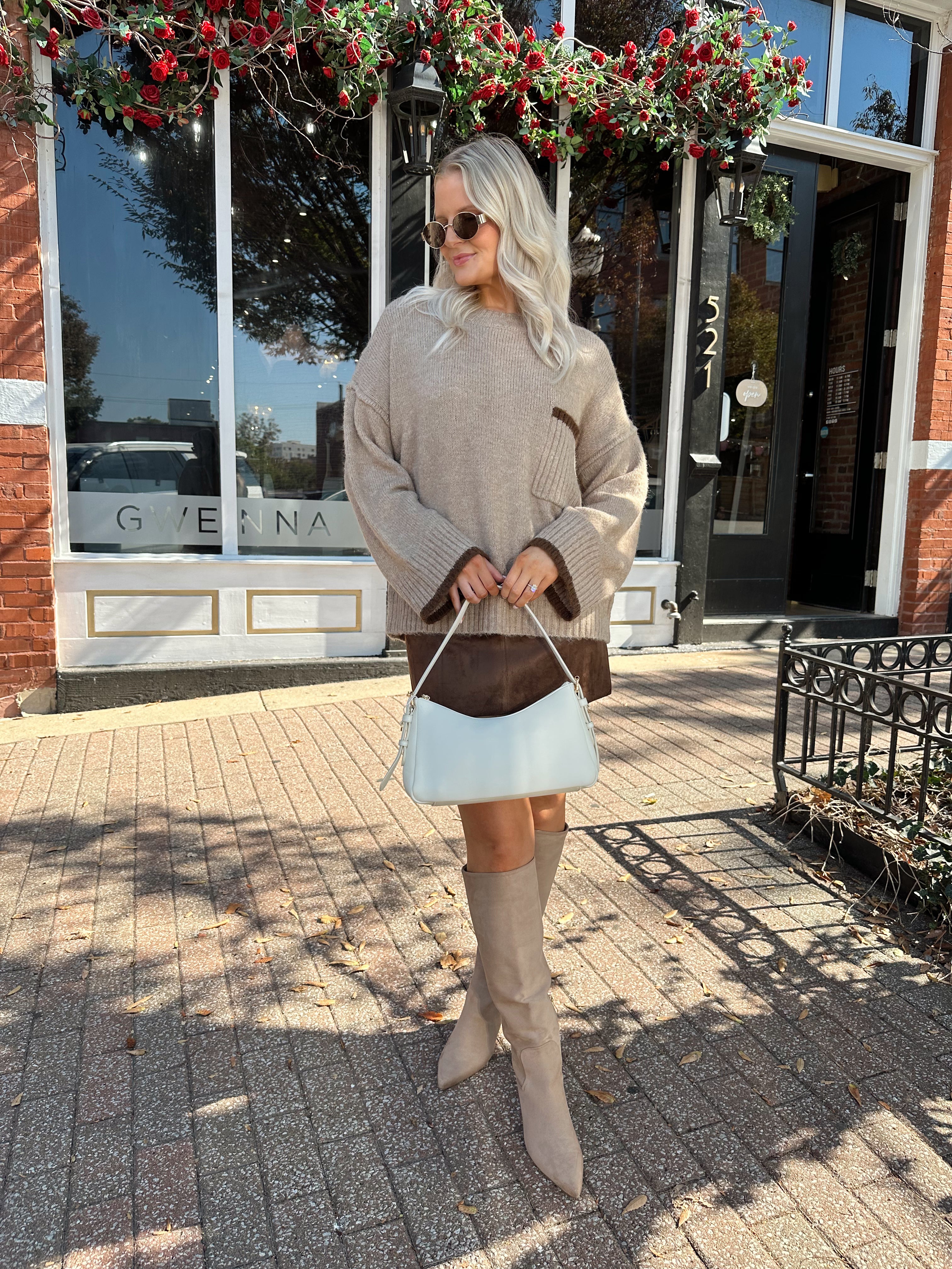 Woman wearing oversized taupe knit sweater with mocha trim detailing.