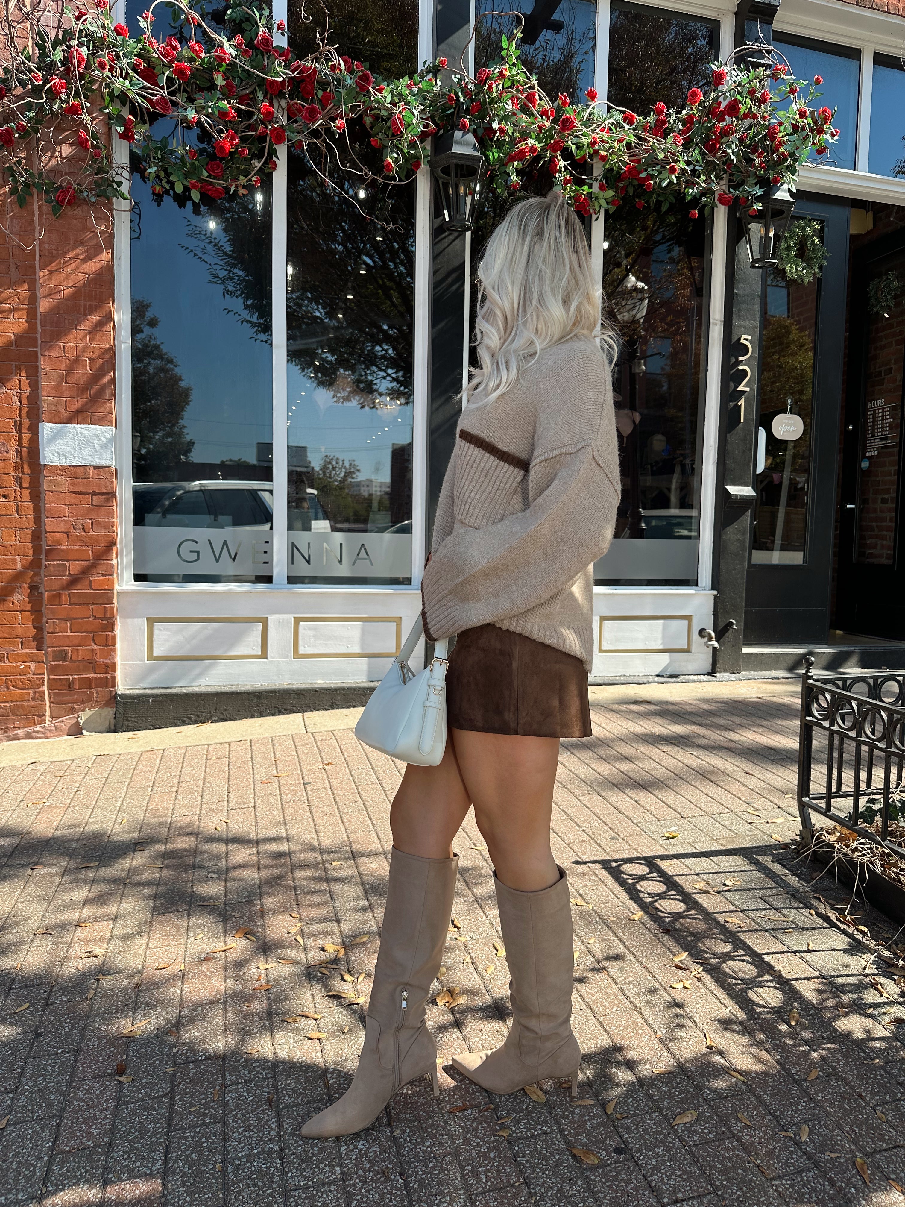 Woman wearing oversized taupe knit sweater with mocha trim detailing.