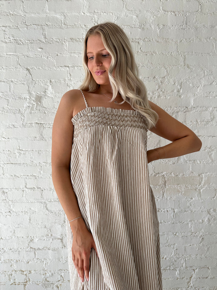 Woman wearing beige striped maxi dress with gathering stitch details.
