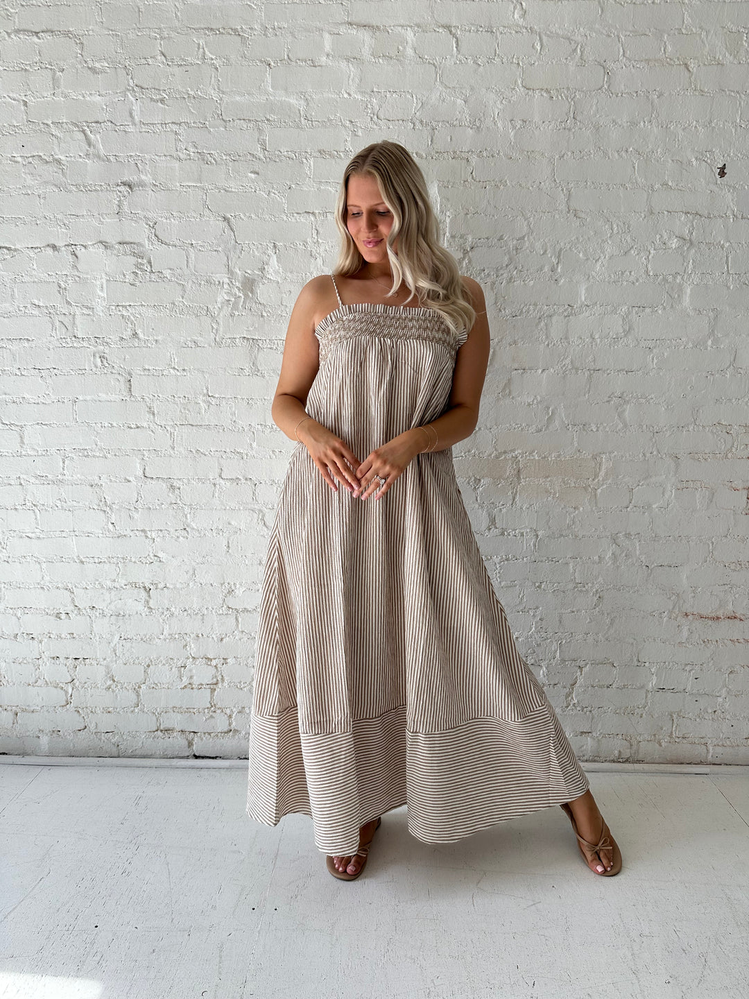 Woman wearing beige striped maxi dress with gathering stitch details.