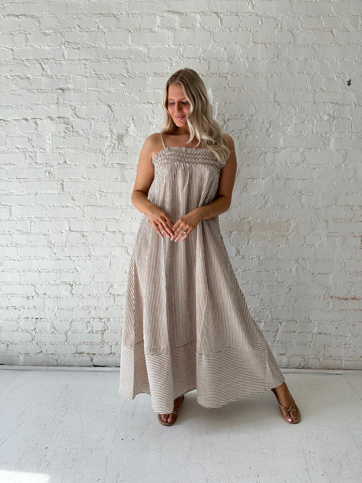Woman wearing beige striped maxi dress with gathering stitch details.