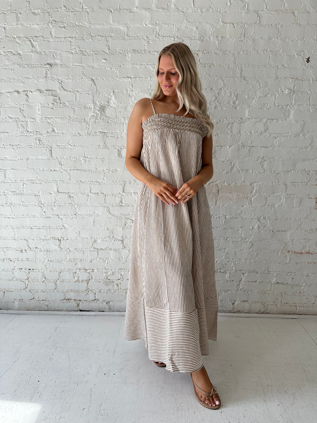 Woman wearing beige striped maxi dress with gathering stitch details.