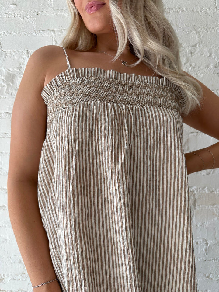 Woman wearing beige striped maxi dress with gathering stitch details.