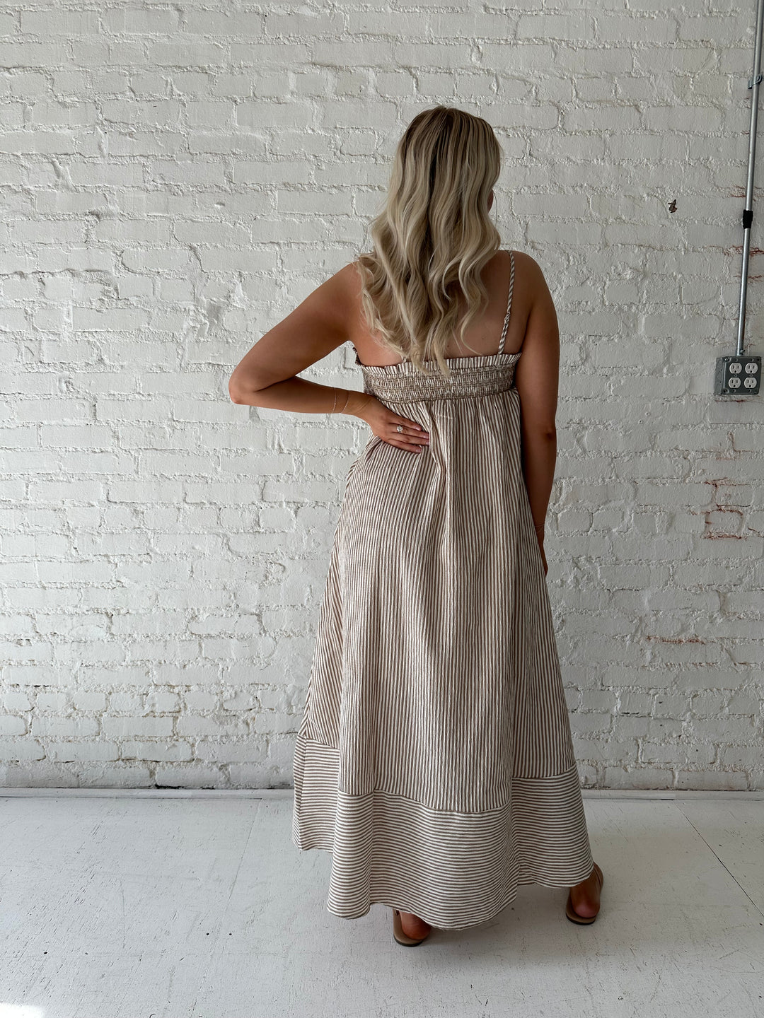 Woman wearing beige striped maxi dress with gathering stitch details.