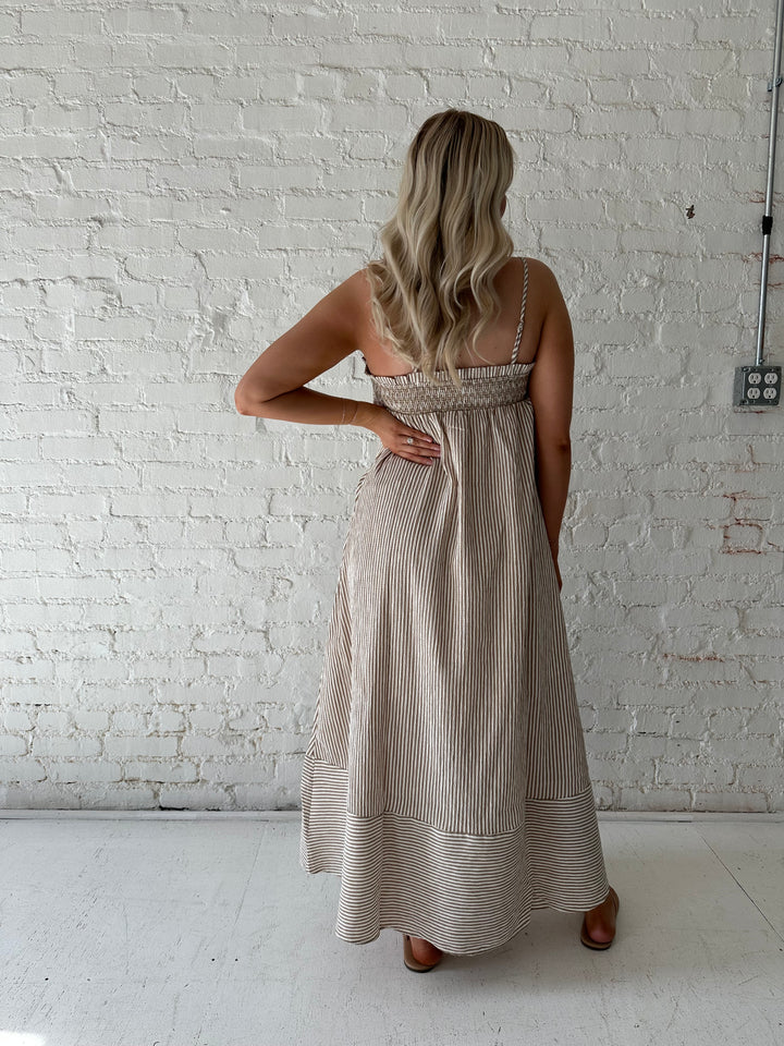 Woman wearing beige striped maxi dress with gathering stitch details.