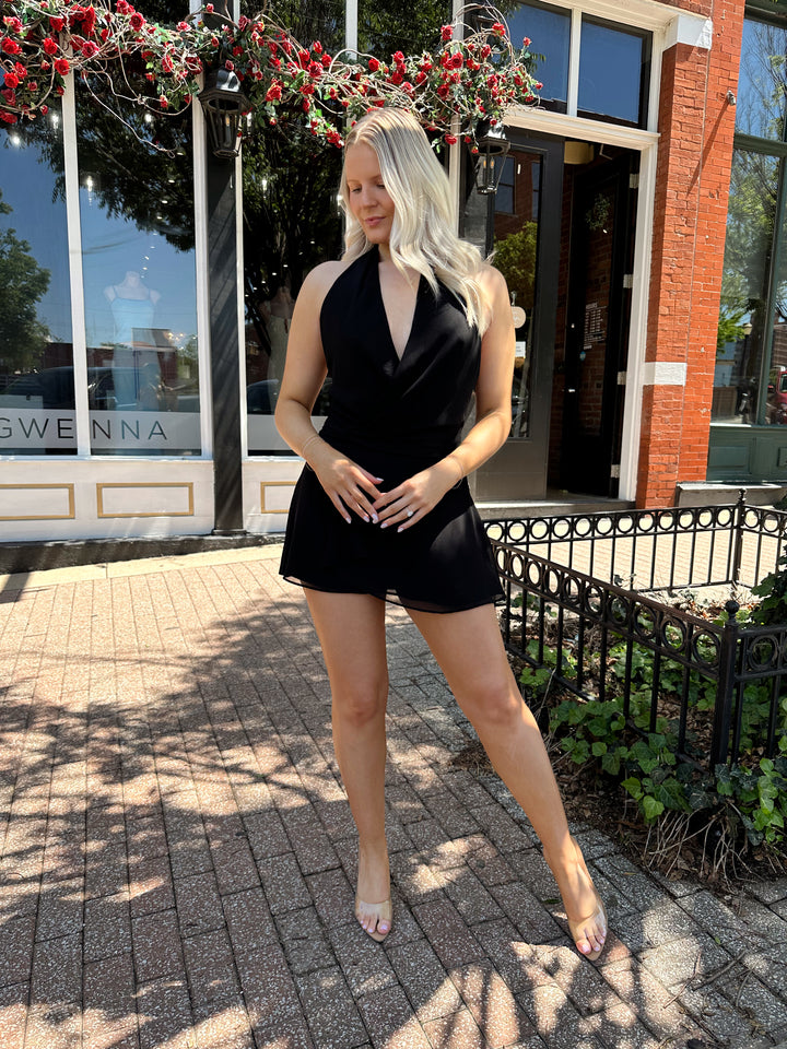 Woman wearing black wrap mini dress with self tie halter neck. 