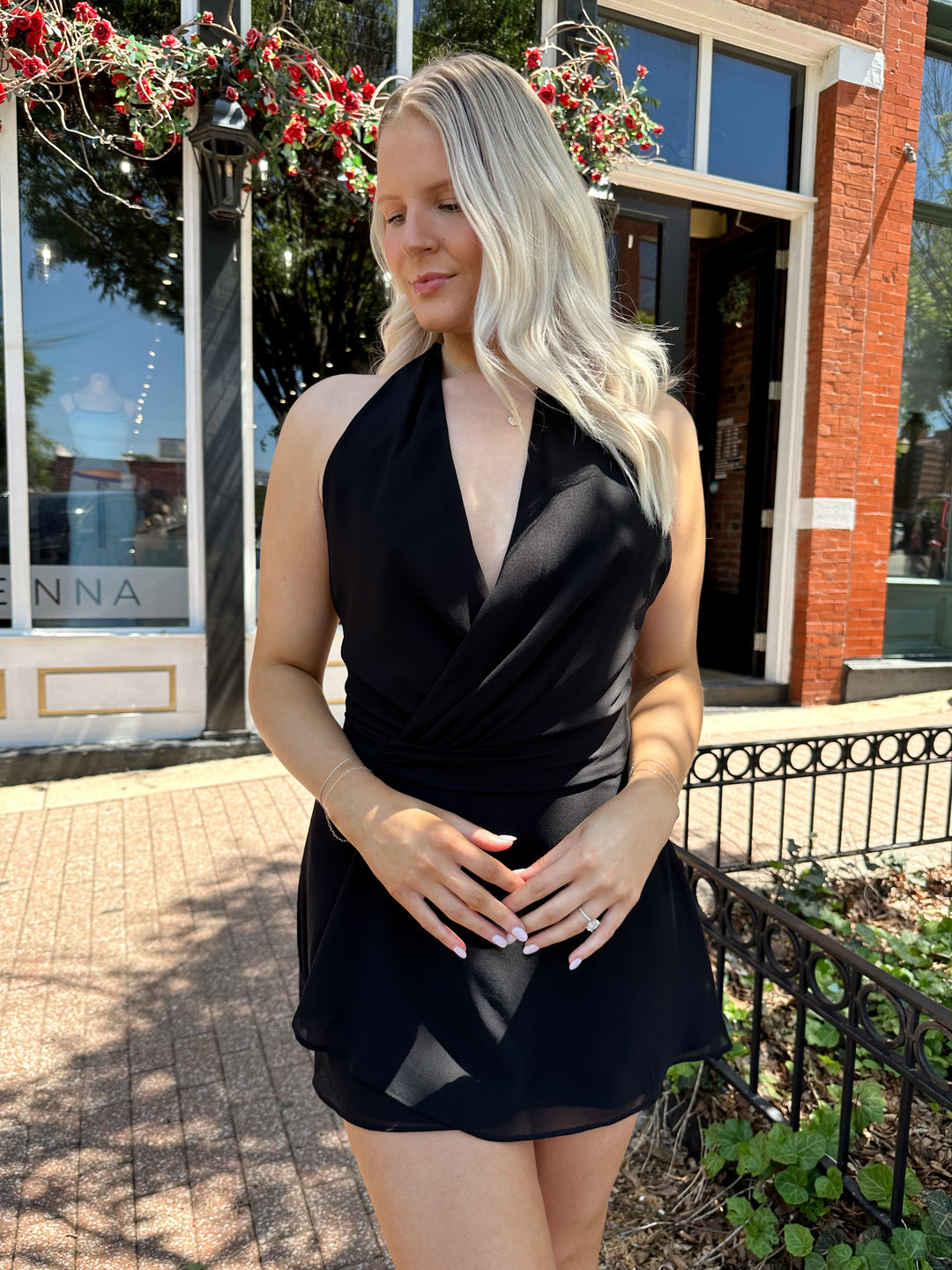 Woman wearing black wrap mini dress with self tie halter neck. 