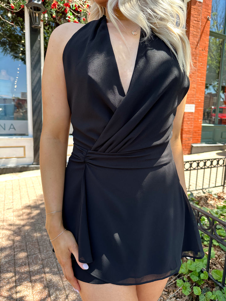 Woman wearing black wrap mini dress with self tie halter neck. 