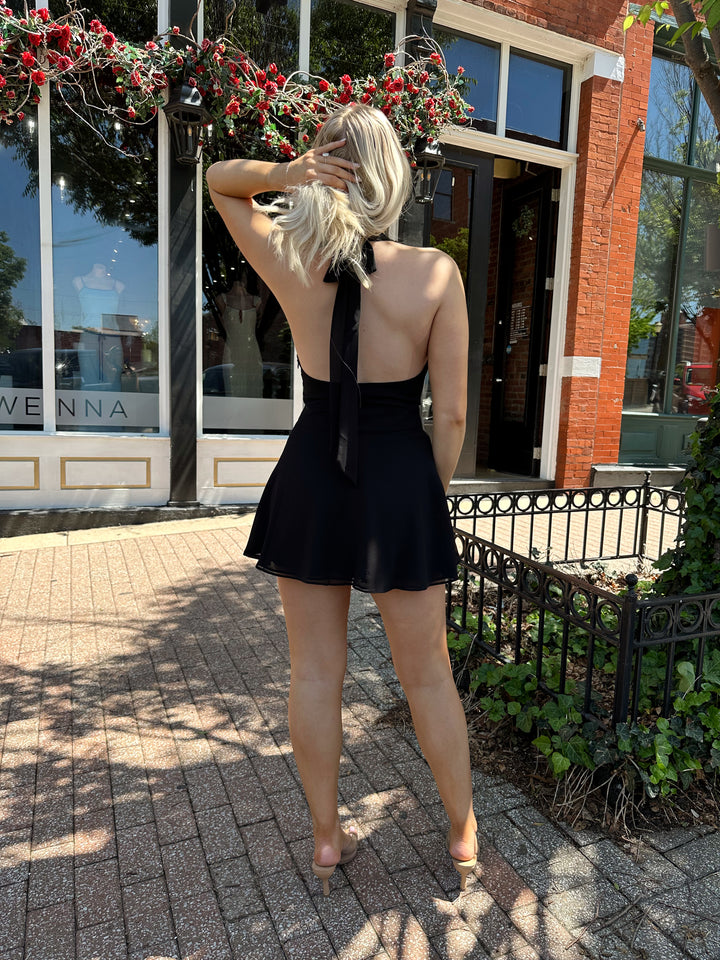 Woman wearing black wrap mini dress with self tie halter neck. 