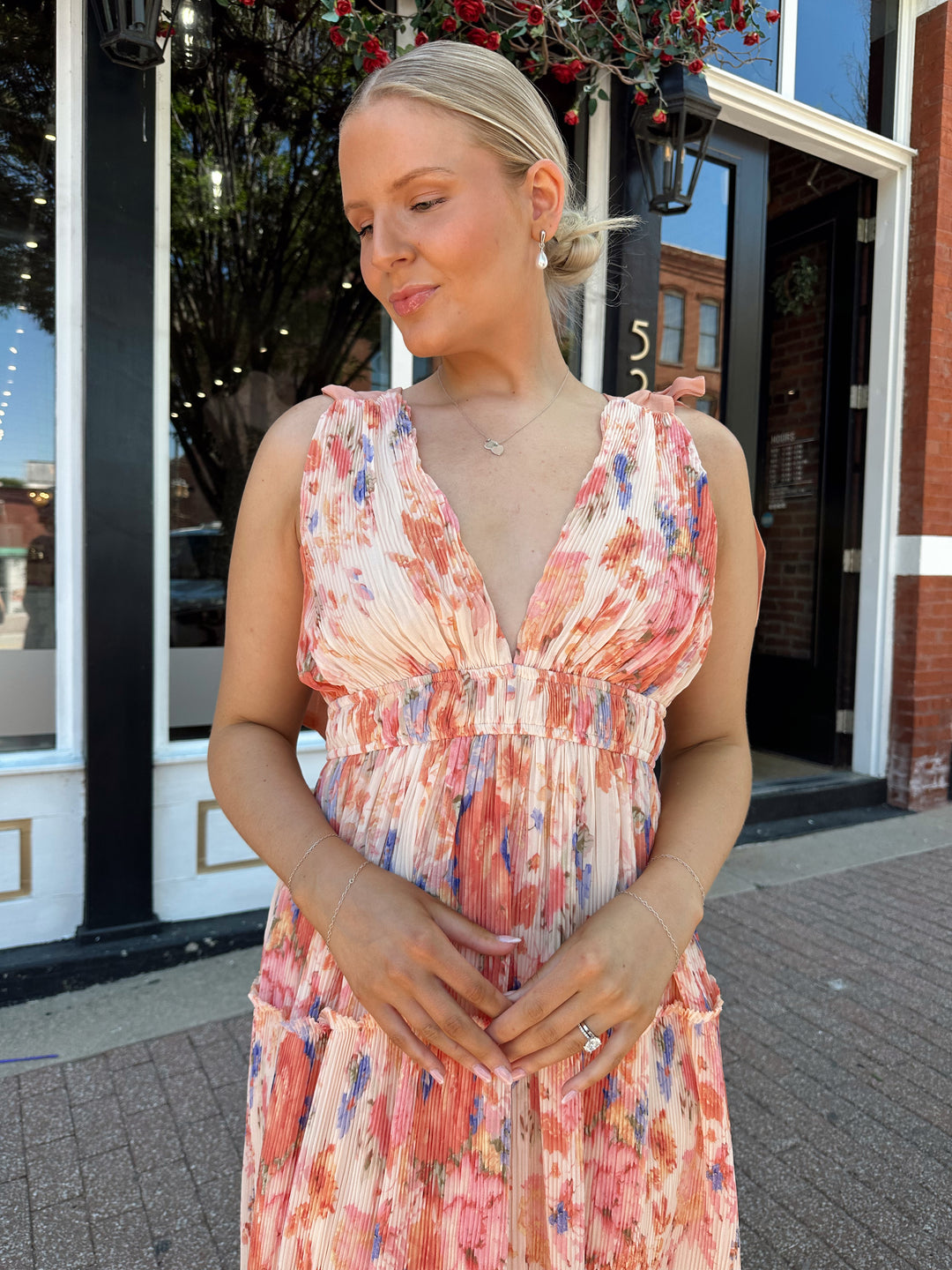 Woman wearing peach multi colored floral, pleated midi dress with v-neckline, and tie strap detail.