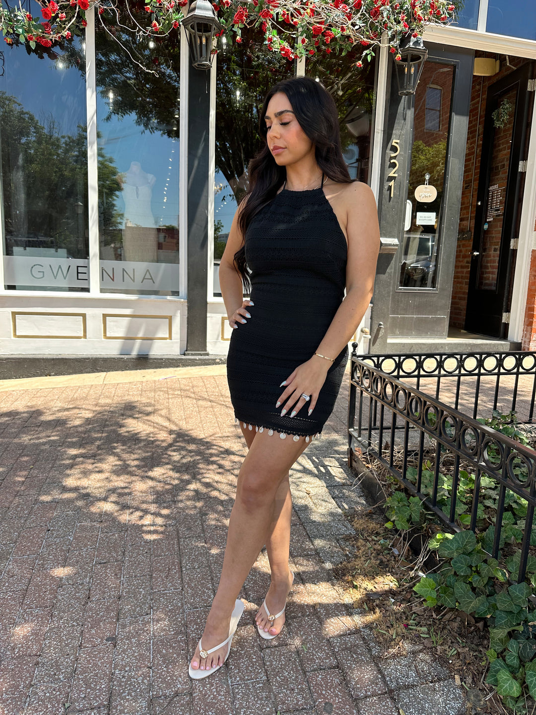 Woman wearing black crochet mini dress with beading hem detail, open back, and self tie straps. 