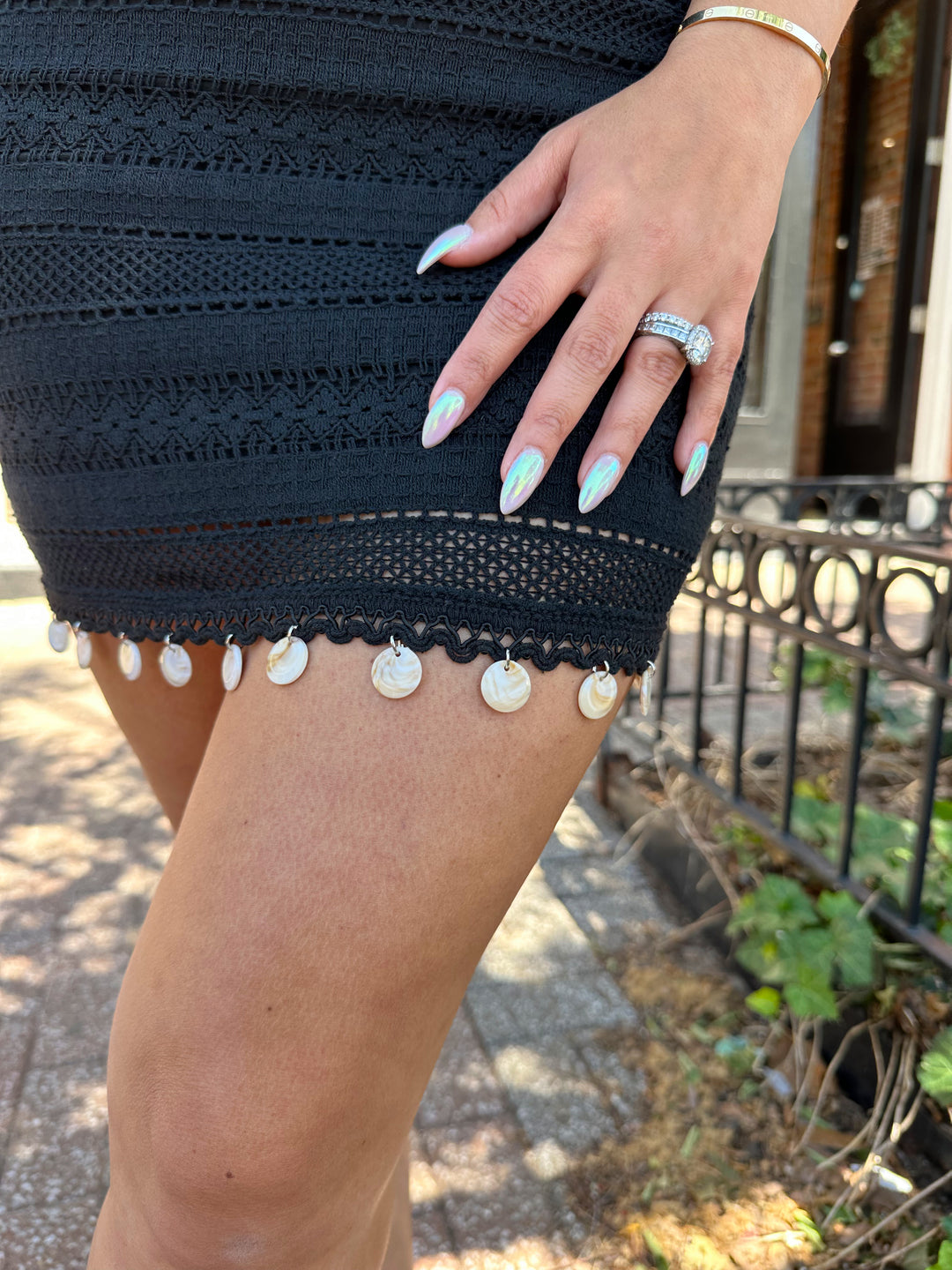 Woman wearing black crochet mini dress with beading hem detail, open back, and self tie straps. 