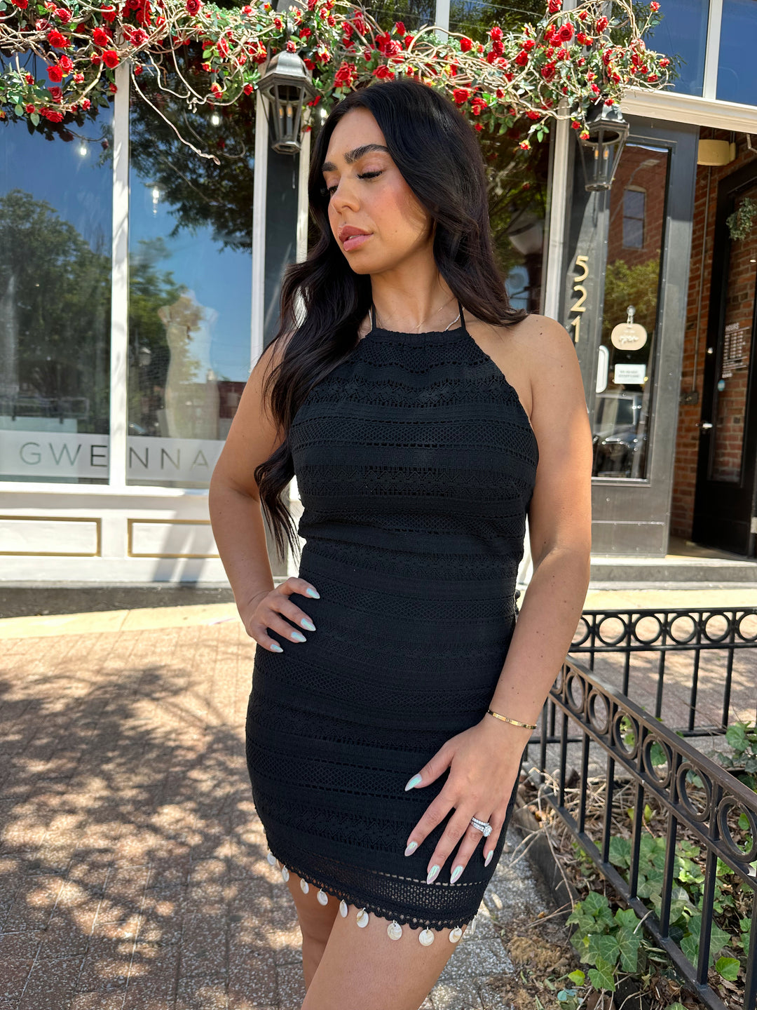 Woman wearing black crochet mini dress with beading hem detail, open back, and self tie straps. 