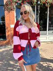 Woman wearing pink and red striped knit front the cardigan and denim skirt.