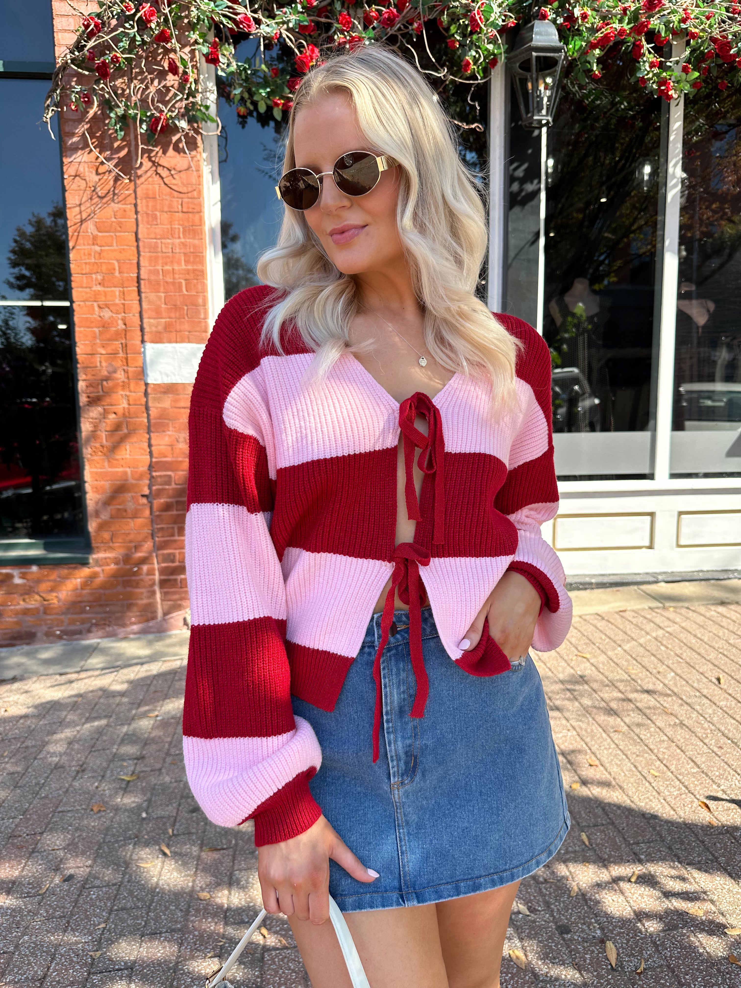 Woman wearing pink and red striped knit front the cardigan and denim skirt.