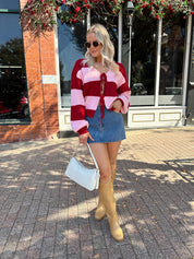 Woman wearing pink and red striped knit front the cardigan and denim skirt.