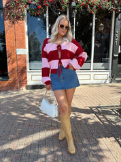 Woman wearing pink and red striped knit front the cardigan and denim skirt.
