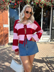Woman wearing pink and red striped knit front the cardigan and denim skirt.