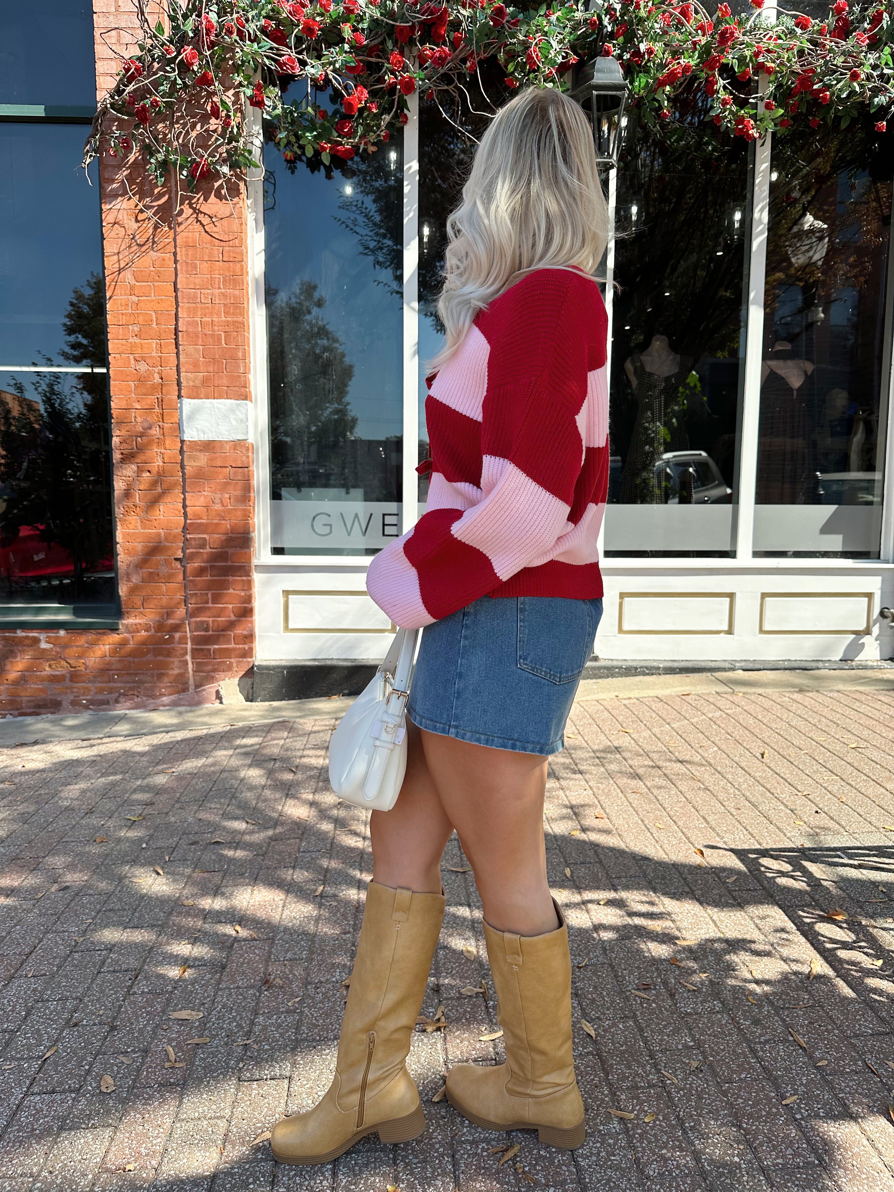 Woman wearing pink and red striped knit front the cardigan and denim skirt.