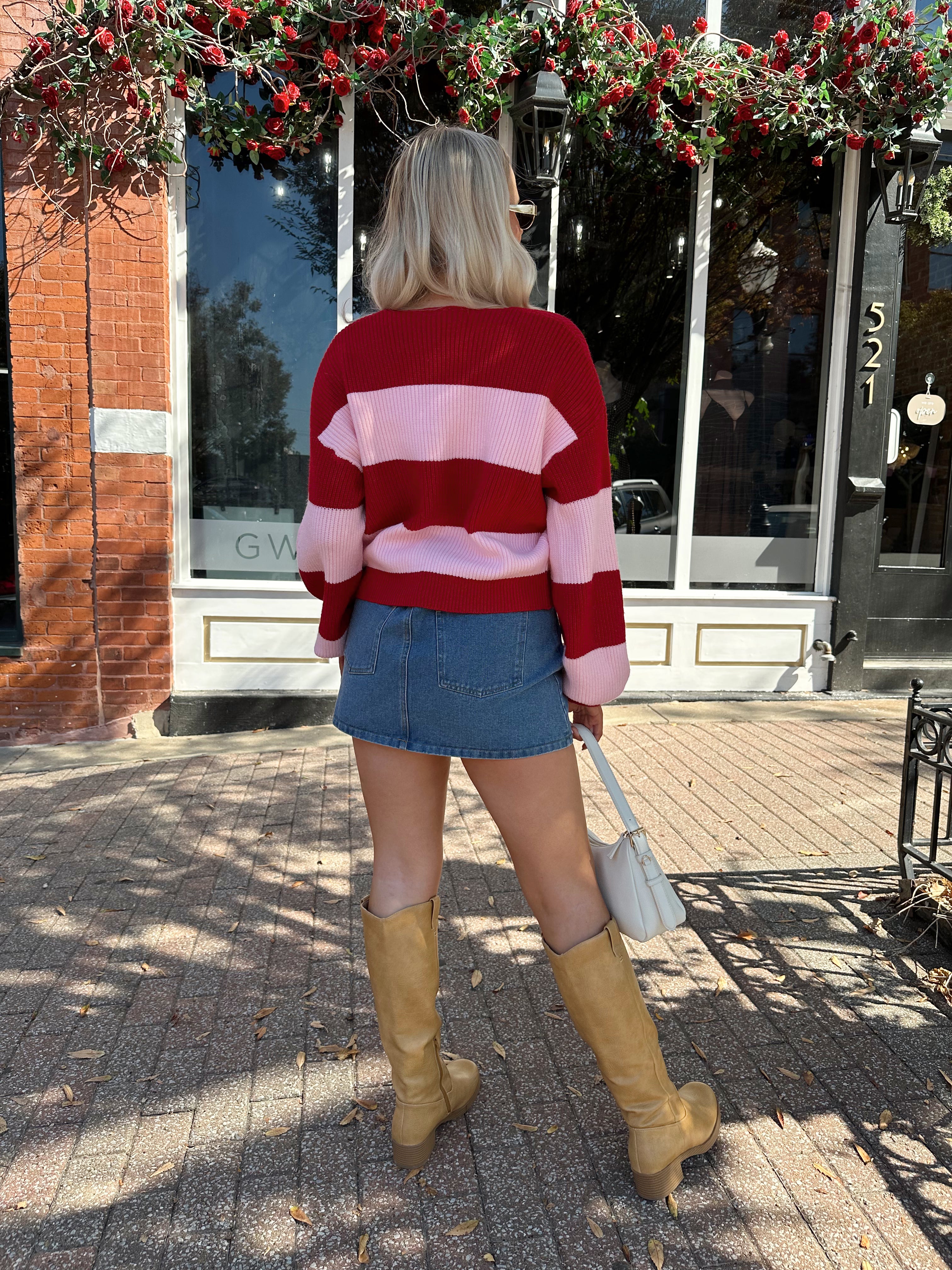Woman wearing pink and red striped knit front the cardigan and denim skirt.