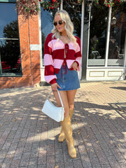 Woman wearing pink and red striped knit front the cardigan and denim skirt.