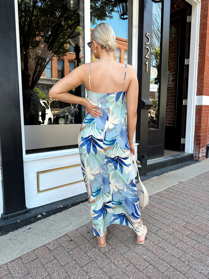 Woman wearing blue and beige tropical print maxi dress with straight neckline, and adjustable spaghetti straps. 