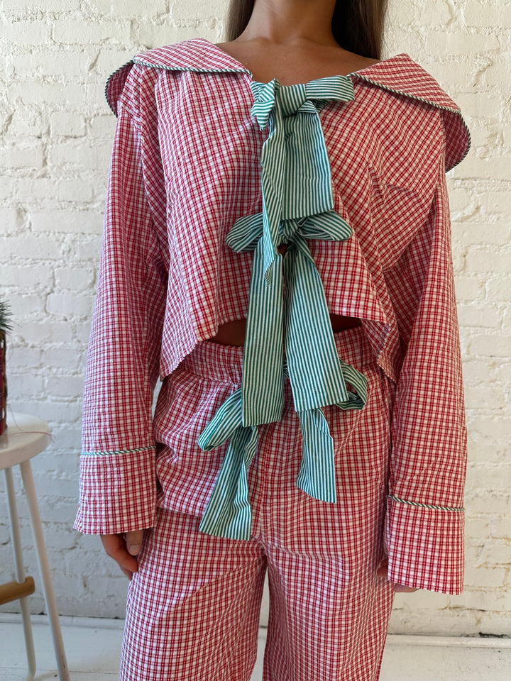Woman wearing red gingham pajama set with front tie closure and collar detail. 