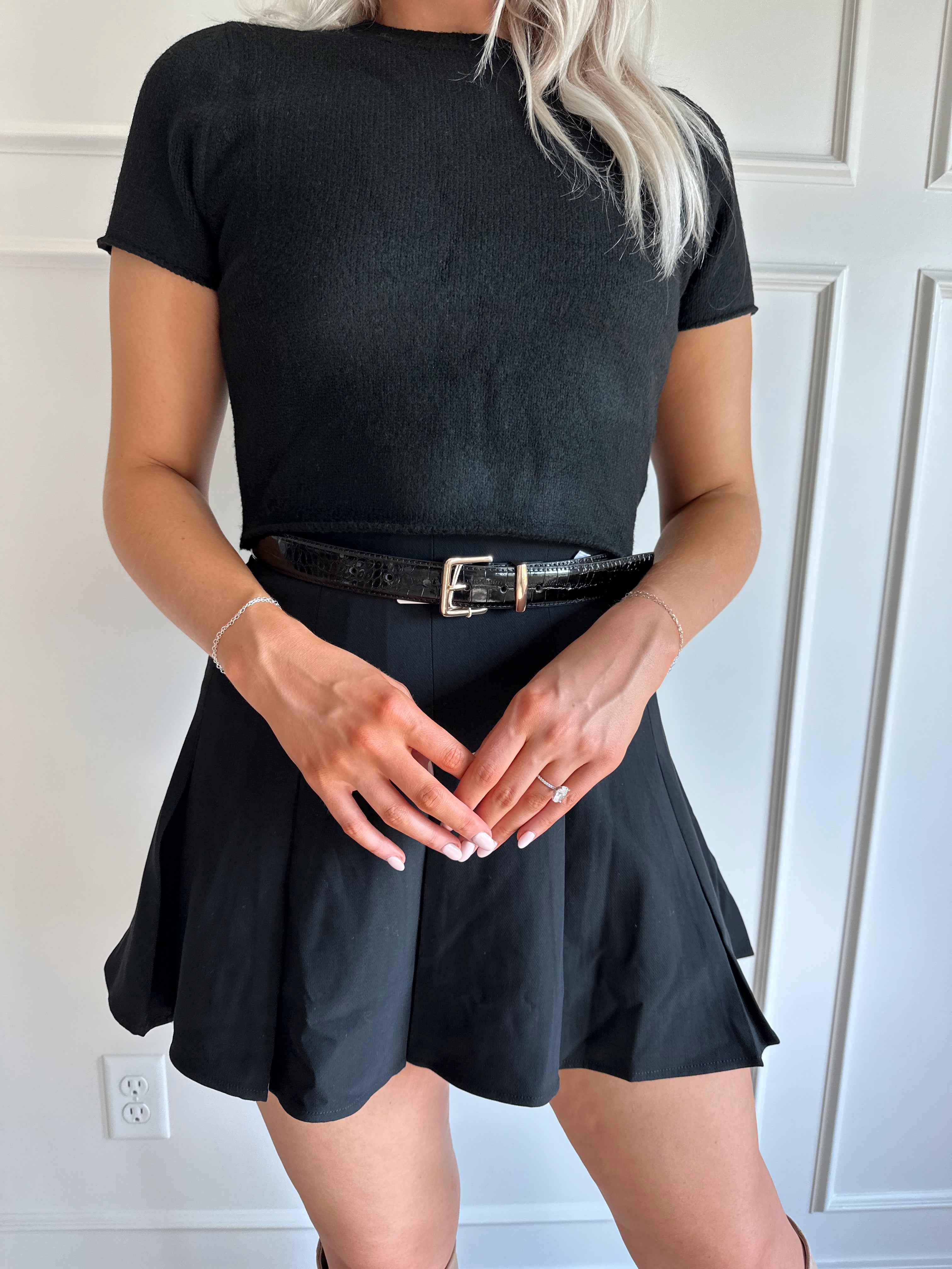 Woman wearing black short sleeve cropped sweater top with black pleated mini skirt. 