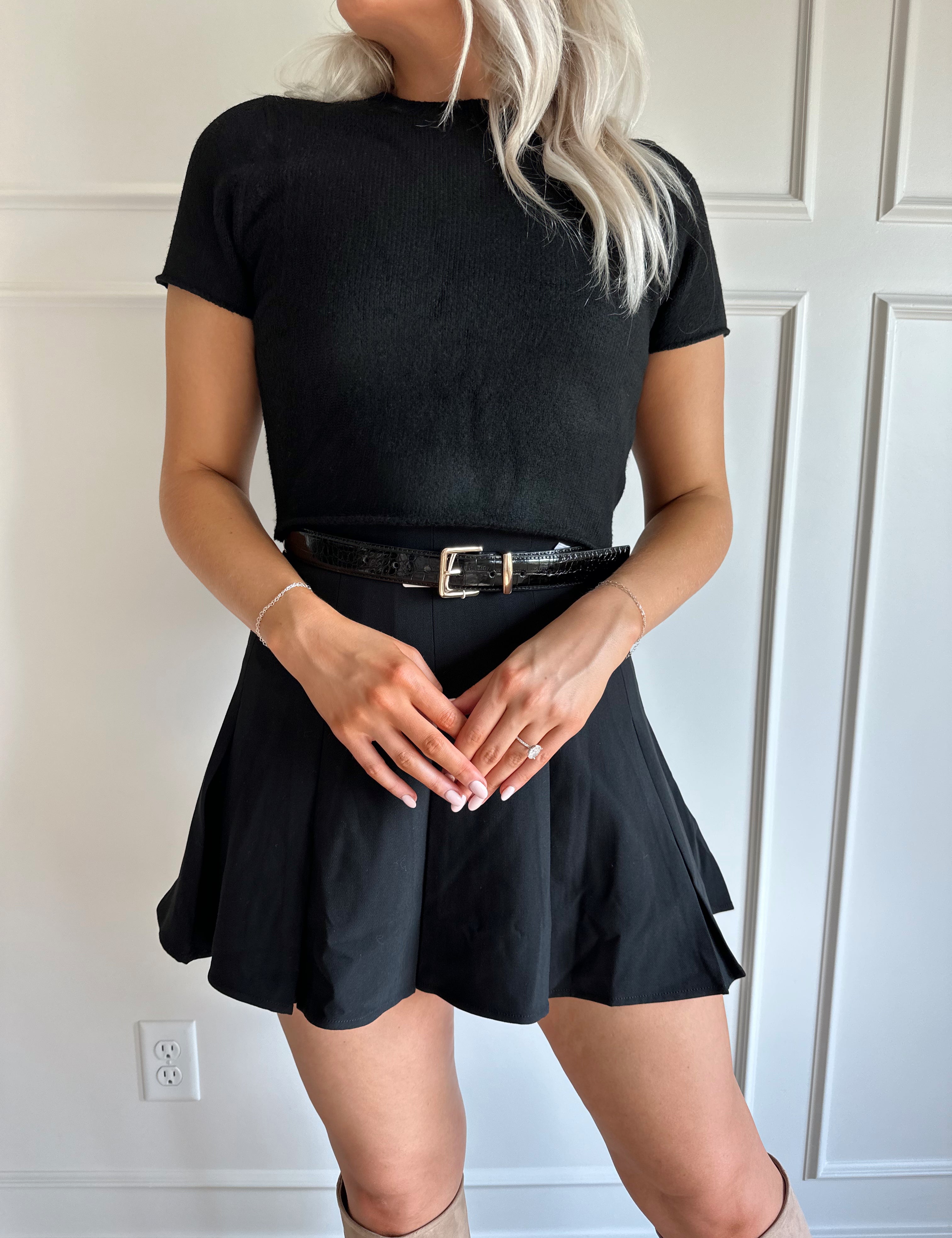 Woman wearing black short sleeve cropped sweater top with black pleated mini skirt. 