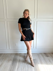 Woman wearing black short sleeve cropped sweater top with black pleated mini skirt. 