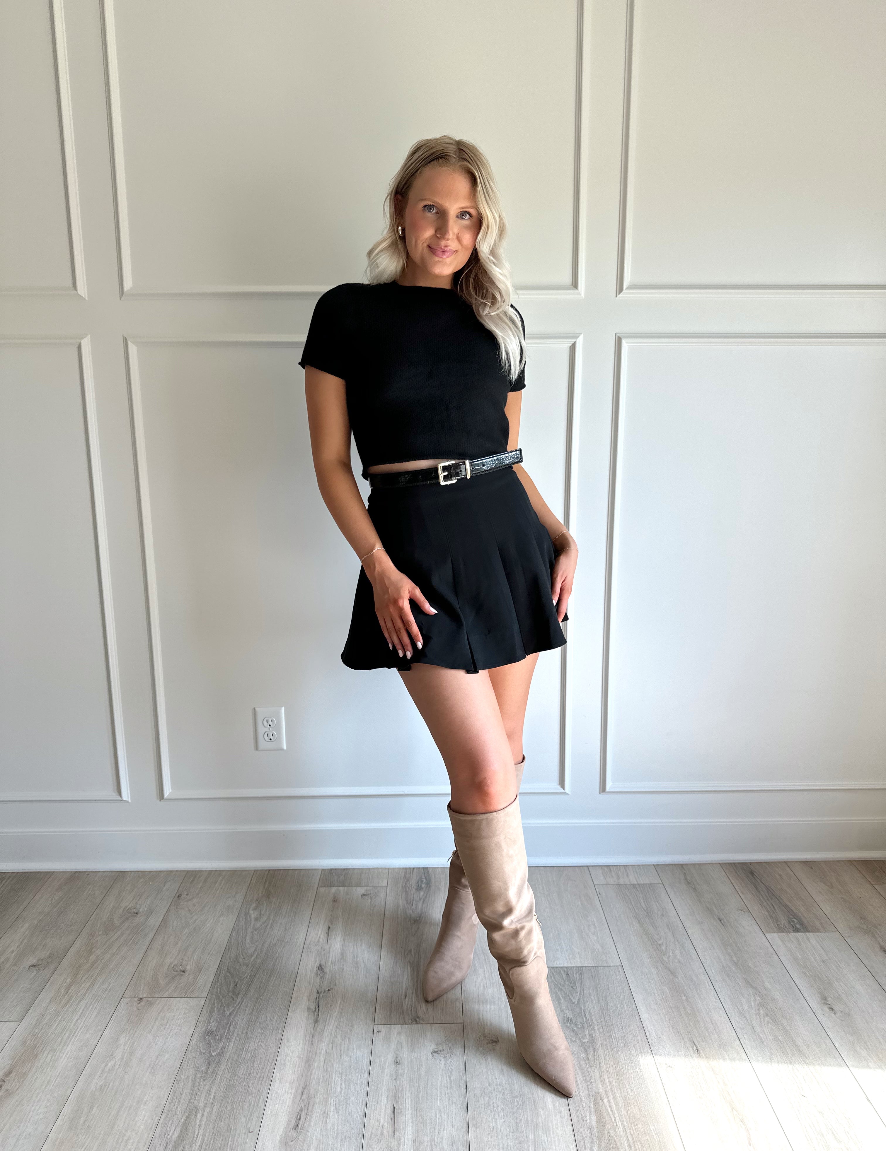 Woman wearing black short sleeve cropped sweater top with black pleated mini skirt. 