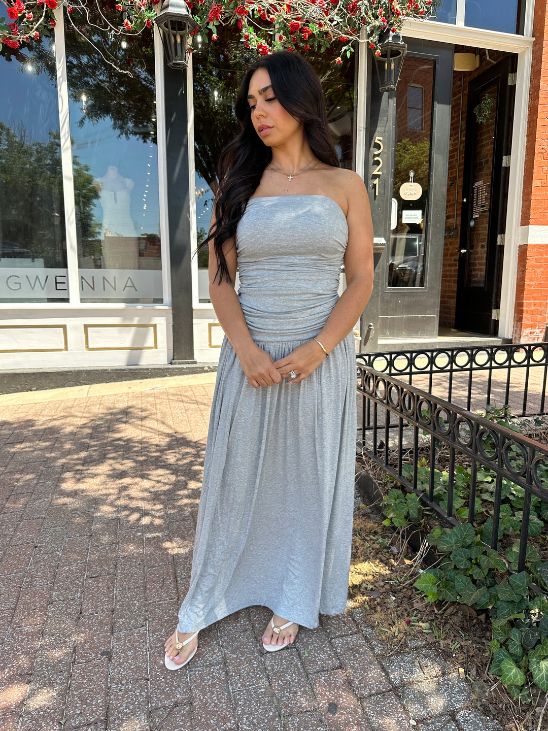Woman wearing grey strapless maxi dress with ruched bodice, and flowy bottom.