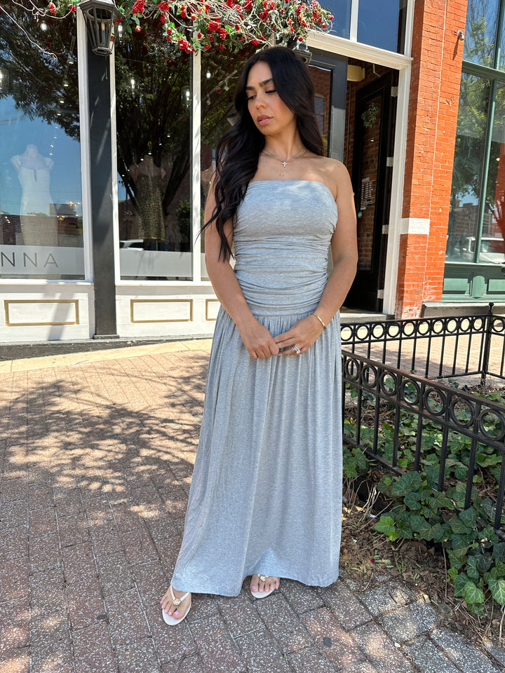 Woman wearing grey strapless maxi dress with ruched bodice, and flowy bottom.