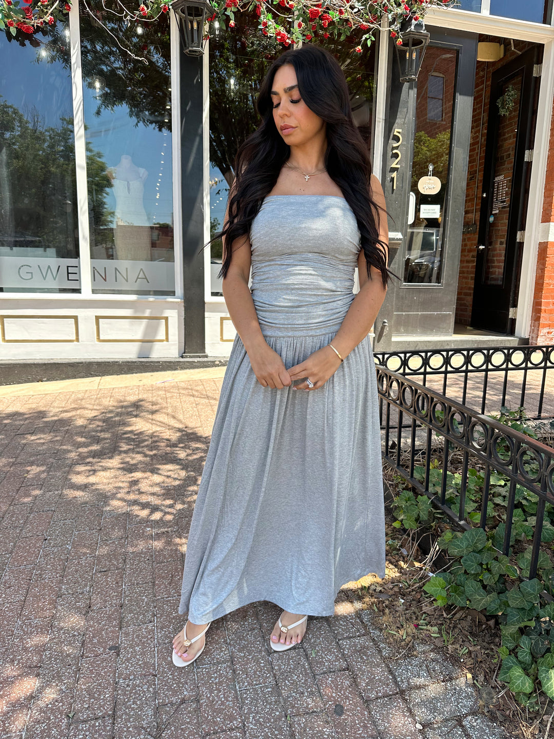 Woman wearing grey strapless maxi dress with ruched bodice, and flowy bottom.