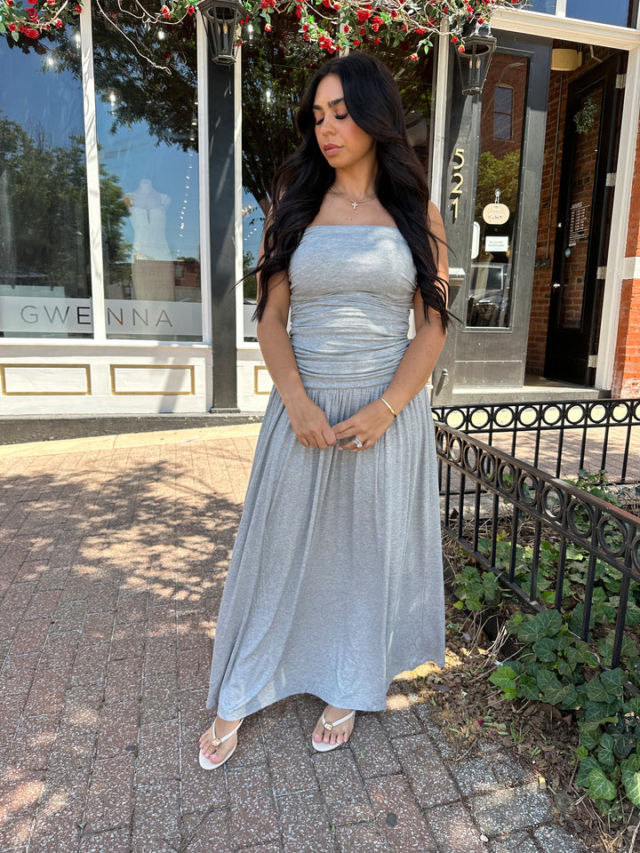 Woman wearing grey strapless maxi dress with ruched bodice, and flowy bottom.
