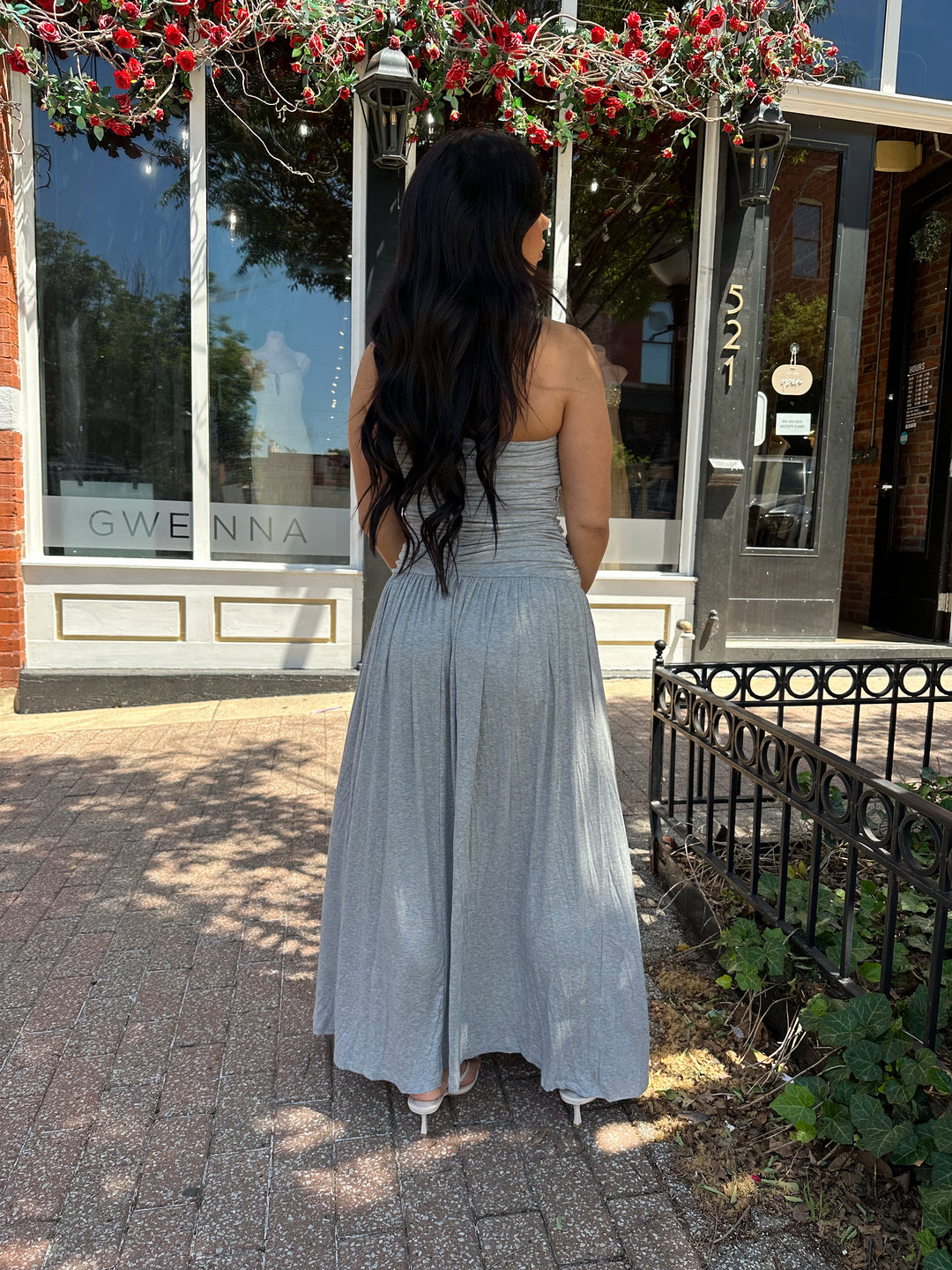 Woman wearing grey strapless maxi dress with ruched bodice, and flowy bottom.