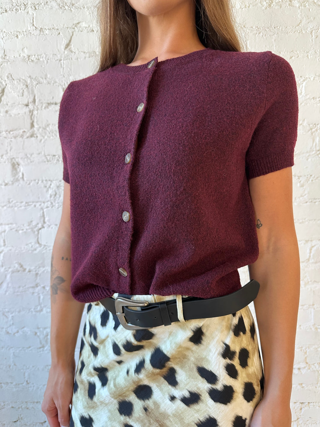 Woman wearing burgundy button down short sleeve cardigan with dark wash jeans. 